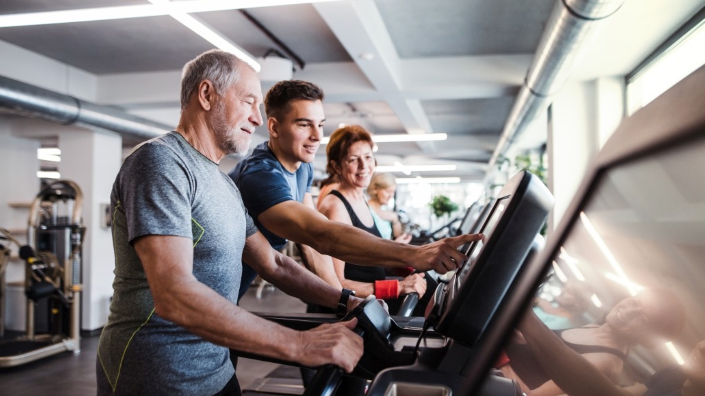 A group of seniors in gym with a young trainer doing cardio work out, exercising on stationary bicycle.