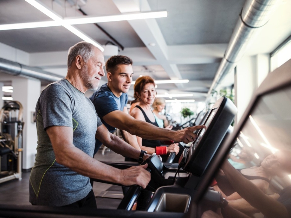 A group of seniors in gym with a young trainer doing cardio work out, exercising on stationary bicycle.