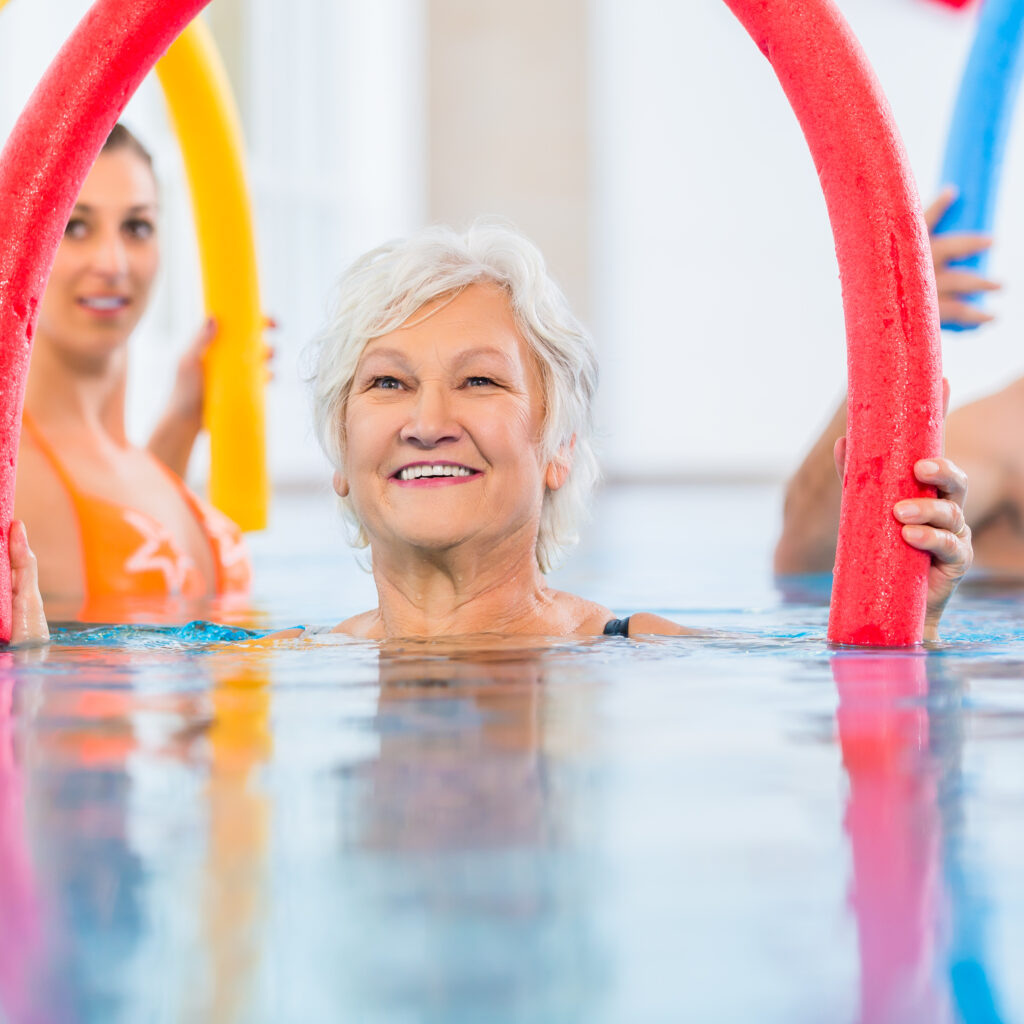 Group  or young and senior people in aquarobic fitness swimming pool exercising with  pool noodle